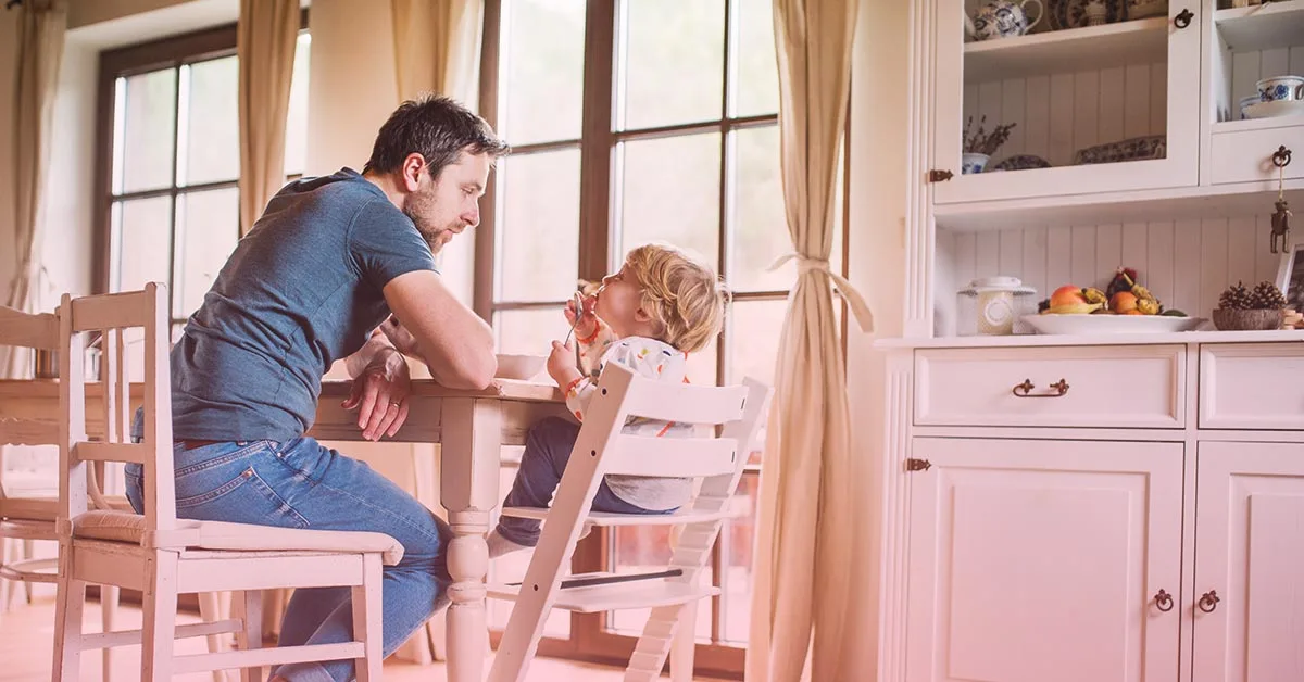 Vater mit Sohn der im Hochstuhl sitzt am Esstisch