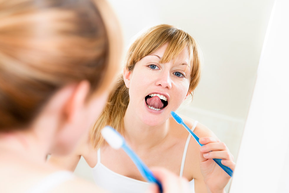 Frau putzt sich vor dem Spiegel im Bad die Zähne